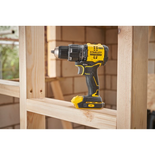 STANLEY SFMCD716B-XJ cordless drill in yellow and black on a wooden frame at construction site.