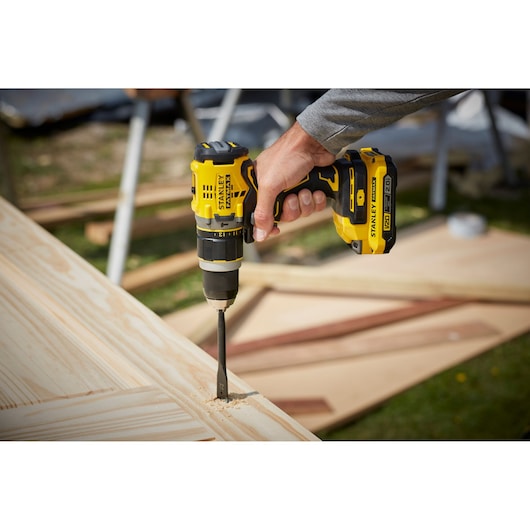STANLEY SFMCD721DR2 yellow cordless drill in use on wood, close-up outdoors.