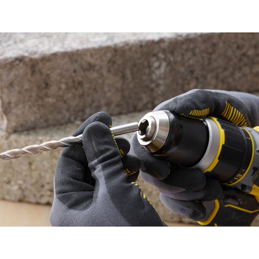 STANLEY SFMCD721DR2 cordless drill close-up, gloved hands inserting drill bit, outdoor setting.