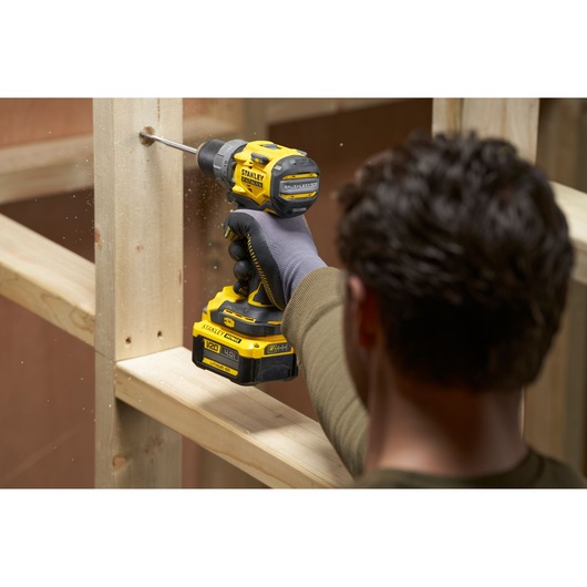 Photo of STANLEY SFMCD725B cordless drill in use drilling into wood, side angle, black and yellow design.