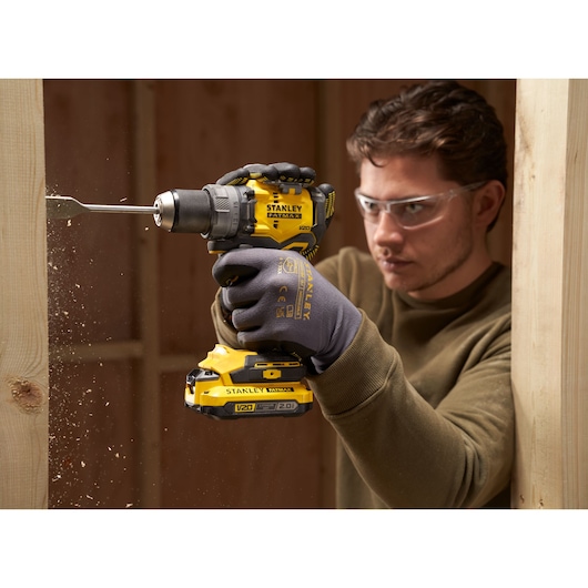 Photo of STANLEY SFMCD725D2K cordless drill in use drilling through wood, close-up view.
