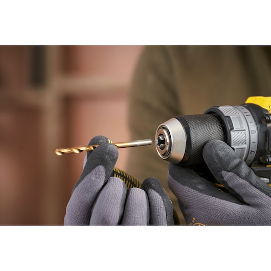 STANLEY SFMCD725D2K drill close-up with gloved hands holding a gold drill bit for insertion.