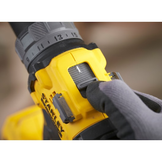 STANLEY SFMCD725D2K drill speed control switch close-up, yellow and black body, gloved hand.