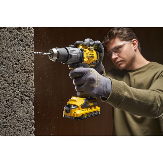 Photo of STANLEY SFMCD726B cordless drill in use, drilling into concrete, close-up on yellow and black tool.