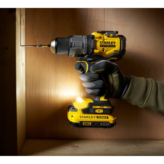 Stanley SFMCD726D2K cordless drill held by gloved hand, drilling into wood, side angle.