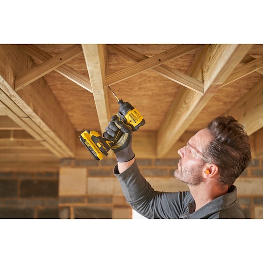 Photo of person using STANLEY SFMCF811B-XJ cordless drill to fasten screw into wooden ceiling frame.
