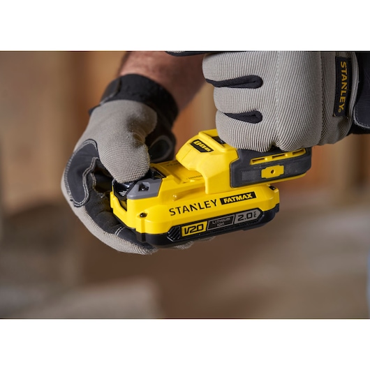 Photo of STANLEY SFMCF820B FATMAX V20 cordless tool battery in gloved hands, close-up view.