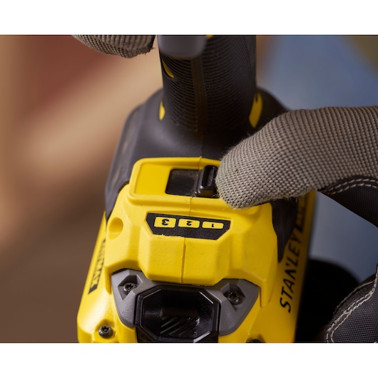 Photo of STANLEY SFMCF820B drill speed controls close-up, yellow and black, gloved hand adjusting settings.