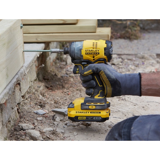 STANLEY SFMCF820B cordless impact driver in use, yellow and black, driving a screw into wood outdoors.