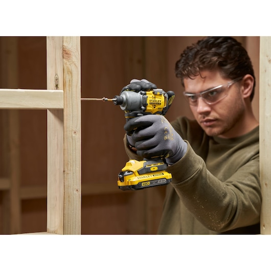 Photo of STANLEY SFMCF830D2K impact driver being used to drive a screw into wood framing, user wearing work gloves.