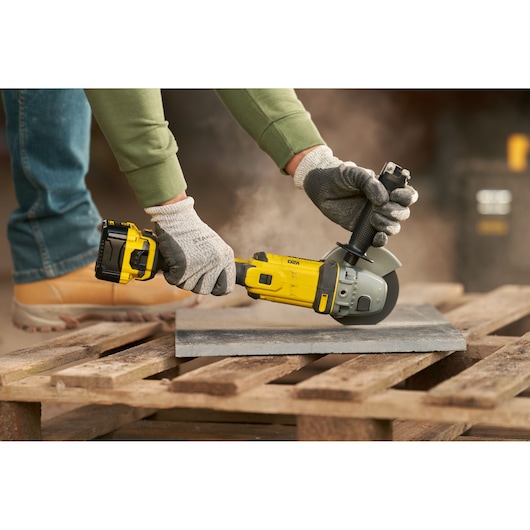 STANLEY SFMCG400B cordless angle grinder in use, cutting a tile on a wooden pallet, close-up side view.