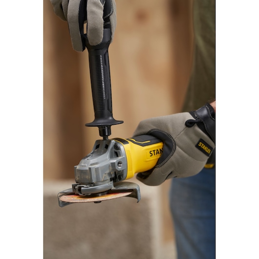 STANLEY SFMCG700B angle grinder held with gloves, photography close-up showing handle and disc.