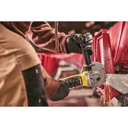 Photo of worker using STANLEY SFMCG700M2K cordless angle grinder on metal frame, sparks flying, close-up action shot.