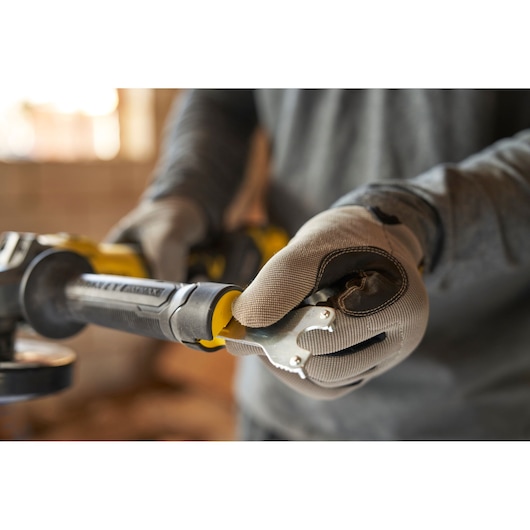 STANLEY SFMCG710B-XJ angle grinder in use, close-up of gloved hands adjusting tool, indoor setting.