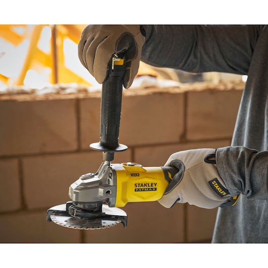 Photo of STANLEY SFMCG710B-XJ cordless angle grinder in use, yellow and black, close-up in construction setting.