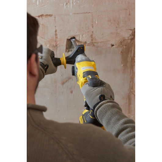 Photo of a person using a STANLEY SFMCH900B demolition hammer on a plaster wall, wearing gloves and safety glasses.