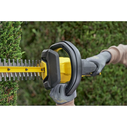 STANLEY SFMCHT650D1 hedge trimmer close-up in use with gloved hands cutting green hedge.