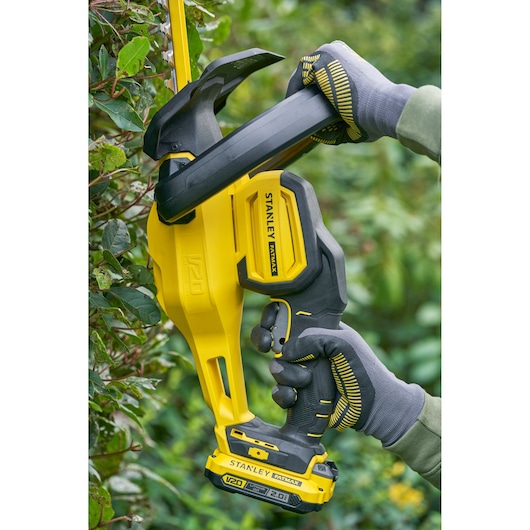 STANLEY SFMCHT650D1 cordless hedge trimmer in use, yellow and black body, trimming green hedge.