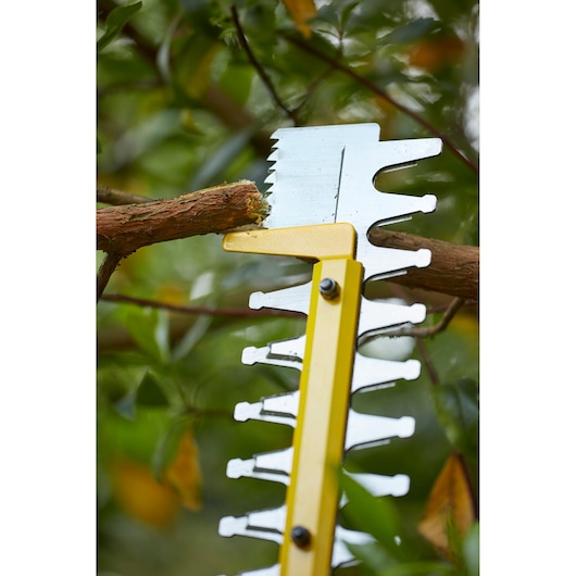 STANLEY SFMCHT855M1 hedge trimmer blade close-up cutting a tree branch outdoors.