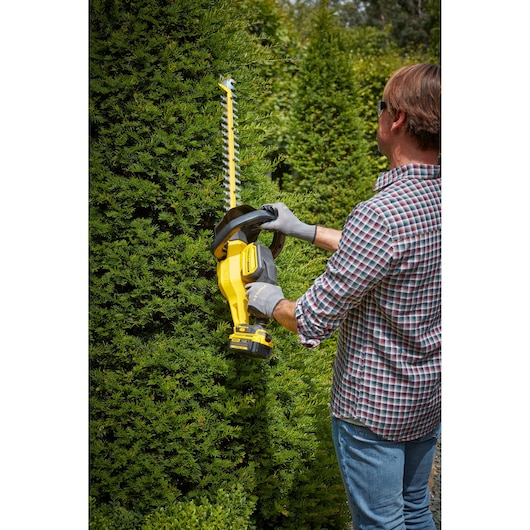 STANLEY SFMCHT855M1 hedge trimmer in use, person trimming green bushes outdoors.