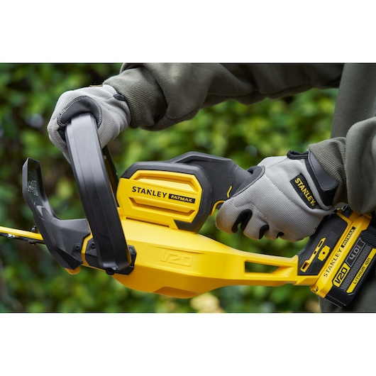 STANLEY SFMCHT855M1 hedge trimmer close-up showing yellow and black body held with gray gloves outdoors.
