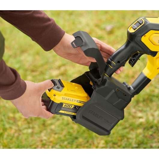 Stanley SFMCPC93B battery being inserted into yellow power tool outdoors, close-up view.