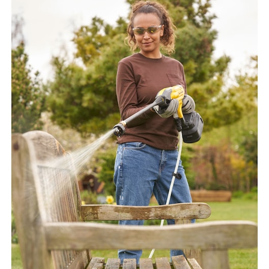 STANLEY SFMCPC93M1 portable pressure cleaner spraying water on wooden bench outdoors.