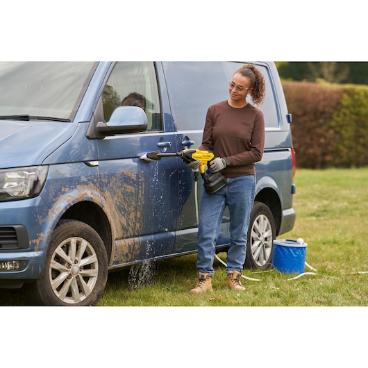 Photo of STANLEY SFMCPC93M1 portable power cleaner used to wash a muddy blue van outdoors.