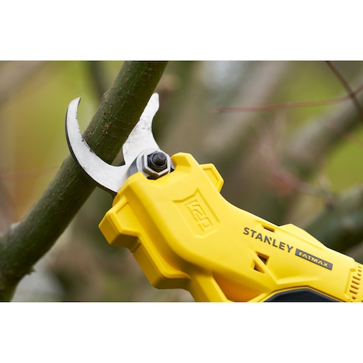 STANLEY SFMCPP32B yellow cordless pruning shears cutting a branch close-up outdoors.