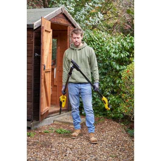 STANLEY SFMCPS720M1 pole saw held outdoors by person in garden near wooden shed.