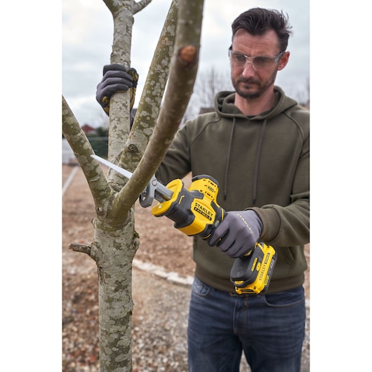 Photo of STANLEY SFMCS305B cordless reciprocating saw being used to cut tree branch outdoors.