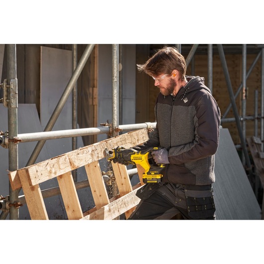 STANLEY SFMCS311B-XJ cordless reciprocating saw cutting wooden pallet outdoors, construction site setting.