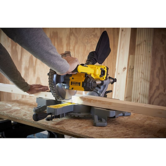STANLEY SFMCS701B miter saw in use, cutting wood plank on a workbench in workshop.