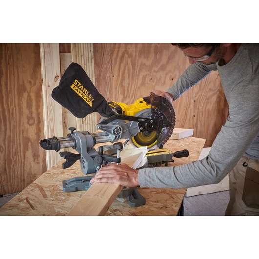 Photo of STANLEY SFMCS701B miter saw cutting wood on a workbench in a workshop setting.