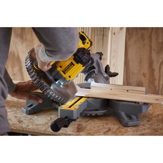 Photo of STANLEY SFMCS701B miter saw cutting wood on workbench, close-up action shot.