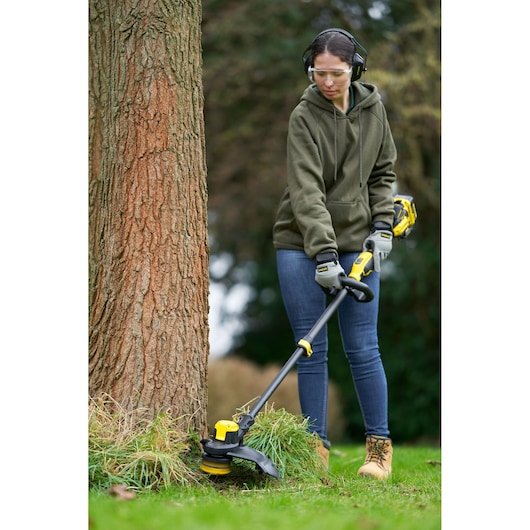 STANLEY SFMCSTB933B string trimmer in use outdoors near a tree, shown with operator wearing safety gear.