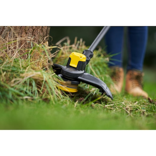 STANLEY SFMCSTB933B grass trimmer close-up, yellow and black, trimming around tree base outdoors.