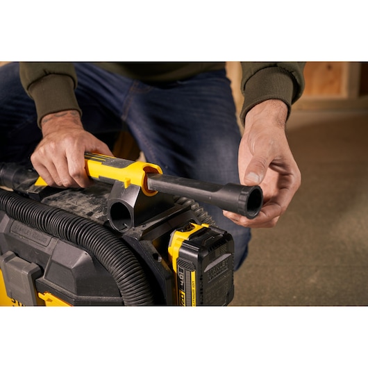 Photo of hands attaching hose to STANLEY SFMCV002B vacuum cleaner, close-up view of connector and battery.