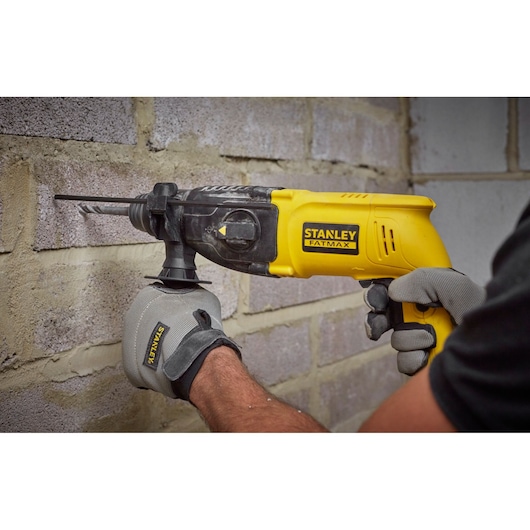 STANLEY SFMEH200K rotary hammer drill in use on masonry wall, yellow and black, close-up photo.