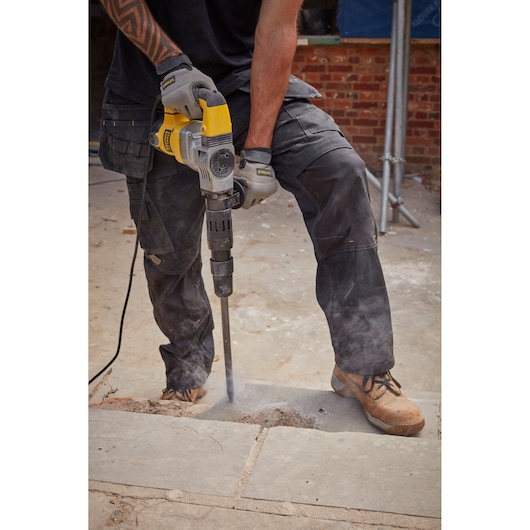 Stanley SFMEH220K-QS demolition hammer in use, breaking concrete outdoors, close-up of tool and worker's hands.