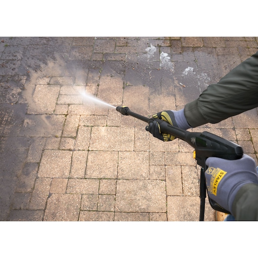 Photo of STANLEY SFMPW2400 pressure washer cleaning patio stones from a side angle.