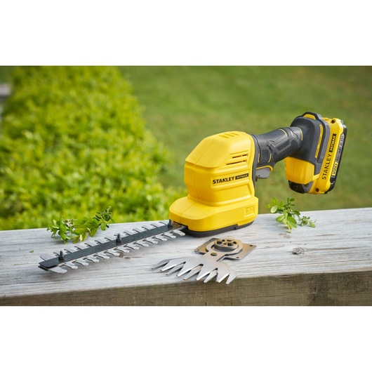 Photo of STANLEY STCSS20B cordless shrub and grass shear with blade attachments on a wooden surface.