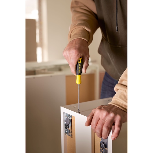 Stanley STHT0-60276 screwdriver used on cabinet, close-up photography, yellow and black handle.