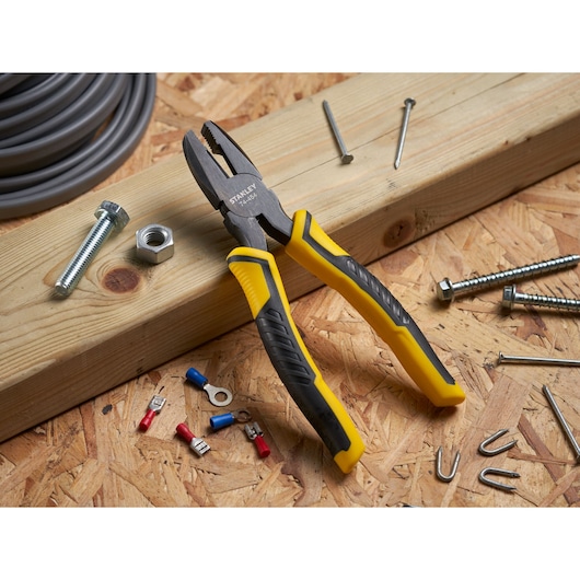 STANLEY STHT0-74367 combination pliers with yellow and black handle on wooden board, surrounded by hardware.