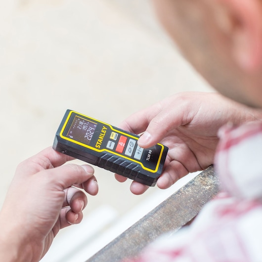 Stanley STHT1-77138 laser distance meter held in hand, showing digital screen and control buttons.