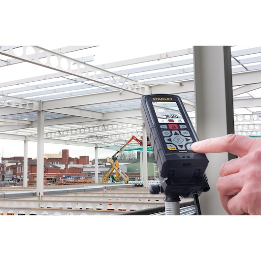 Stanley STHT1-77347 laser distance measurer on tripod in construction site, person pressing button.