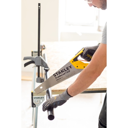 Photo of STANLEY STHT20348-0 hand saw in use cutting a black pipe on a workbench, gloved hand holding pipe.