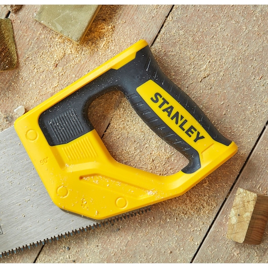 STANLEY STHT20351-1 hand saw with yellow and black handle, close-up on wood and sawdust.