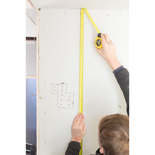 STANLEY STHT36809-0 tape measure used vertically on wall by a person, construction setting, close-up.