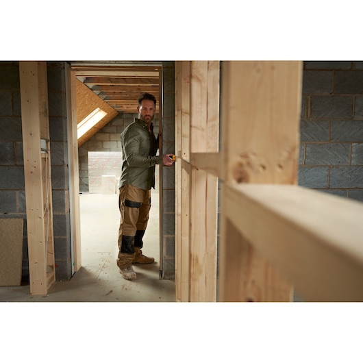 STANLEY STHT77065-0 photography of worker using tape measure in unfinished wooden framed room.
